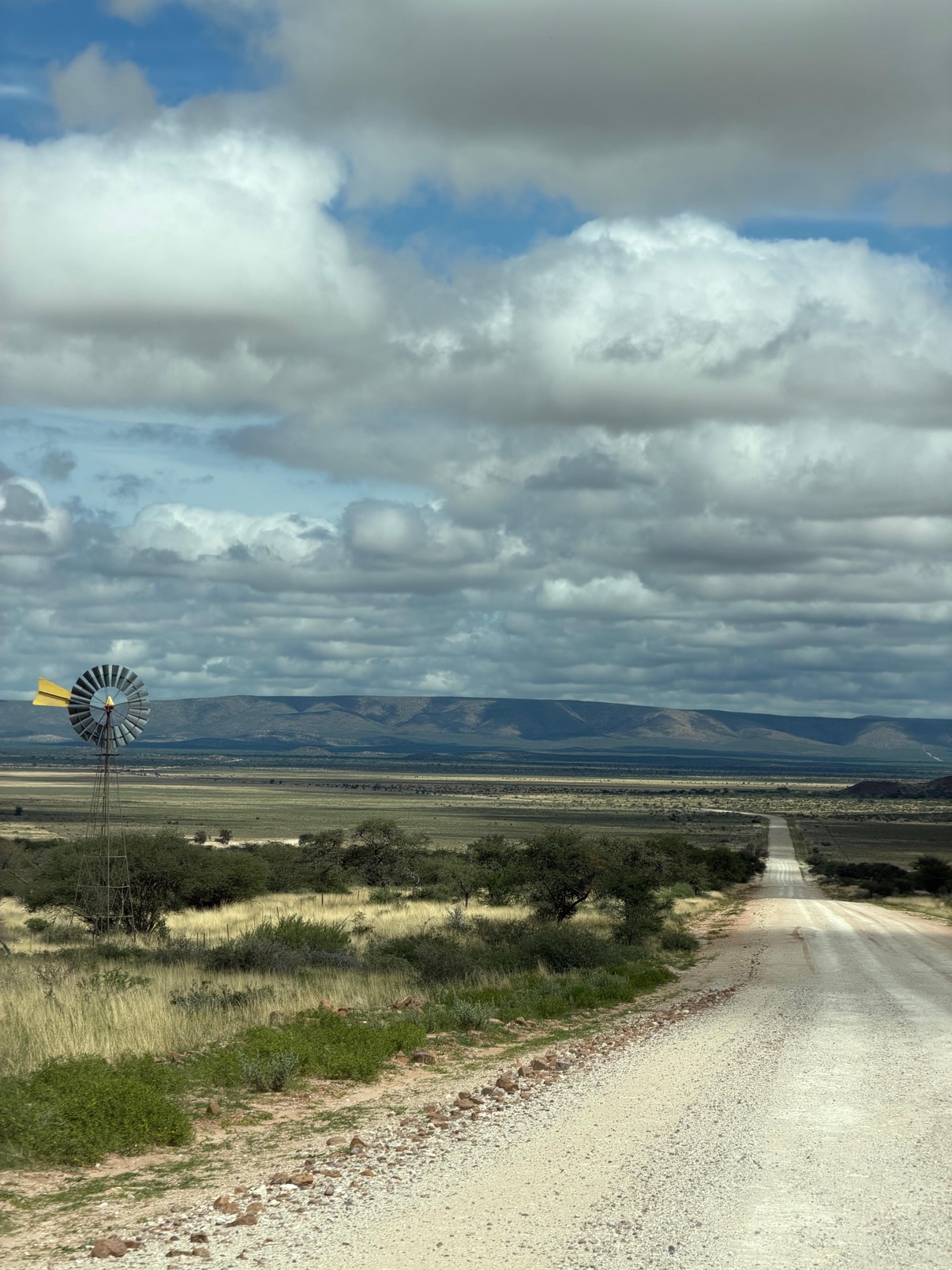A classic windmill beside a gravel road on Zania Farm, with mountains and storm clouds behind